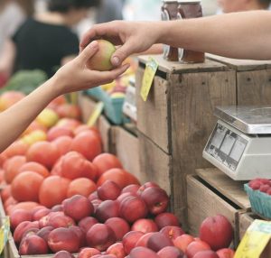a vendor at a farmer's market sells an apple to a customer